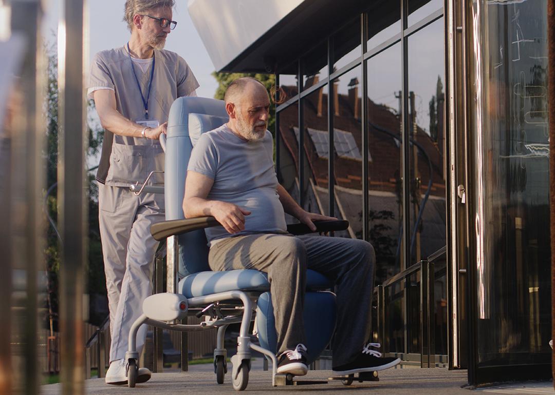 Two doctors assisting a disabled elderly man to the clinic entrance.