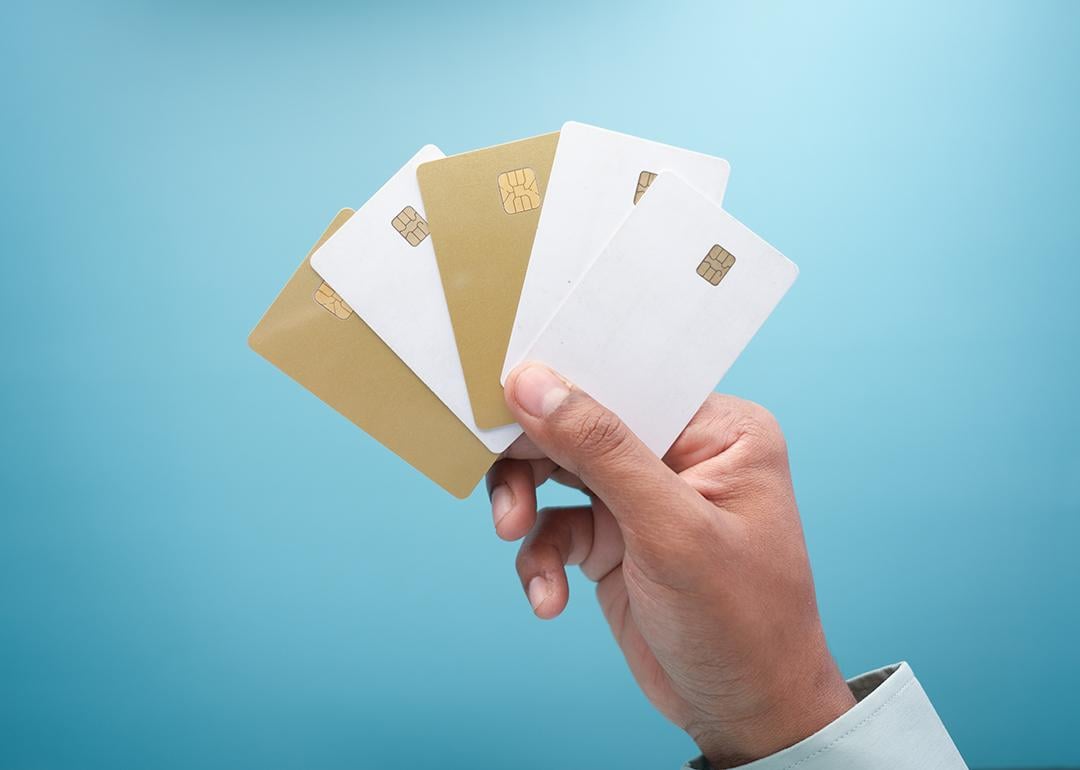 A hand holding an assortment of five gold and white credit card against a blue background.