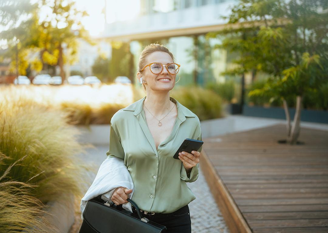 A businesswoman heading to work with a briefcase and listening to wireless earphones.