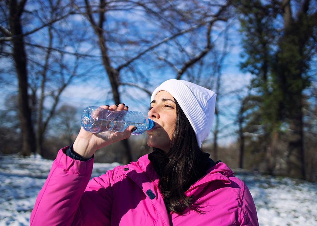 A female athlete in winter clothes drinking water outdoors.