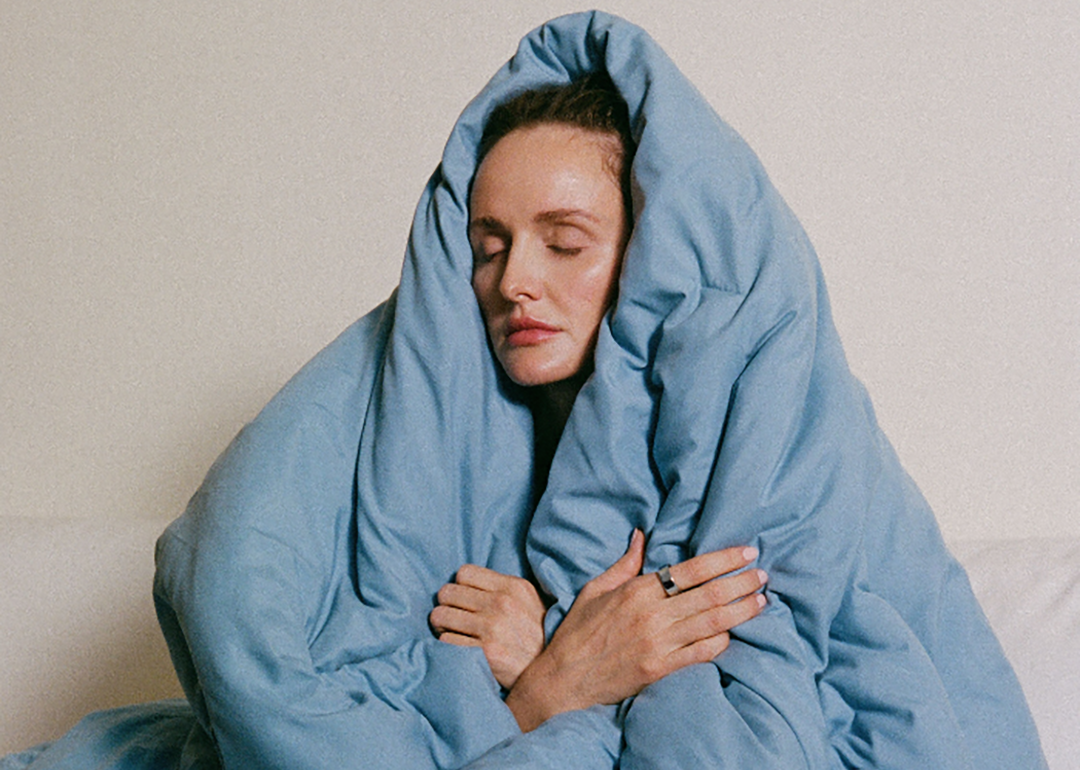 A sleepy woman covering her head with a blue blanket.
