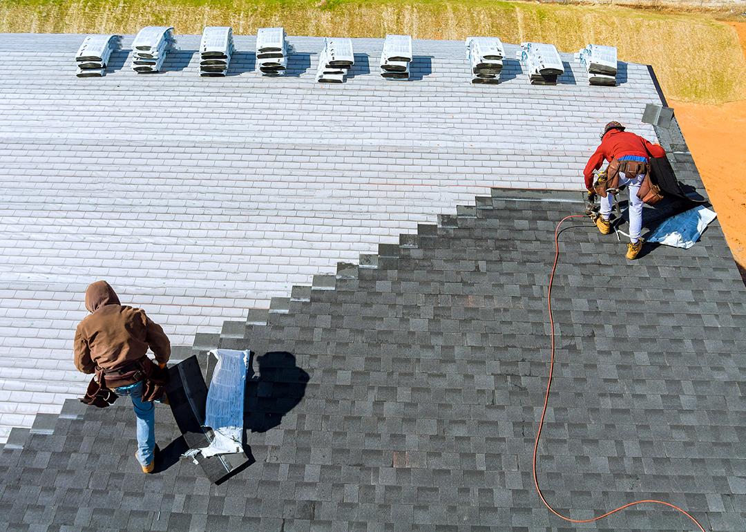 Aerial view of roof workers installing shingles using hammer and nail.