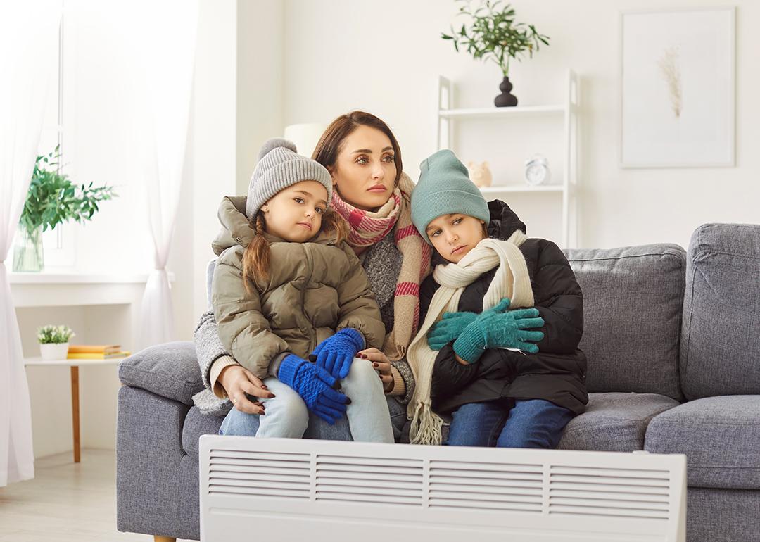 A mother with her two children in winter clothing sitting on a sofa in a cold living room.