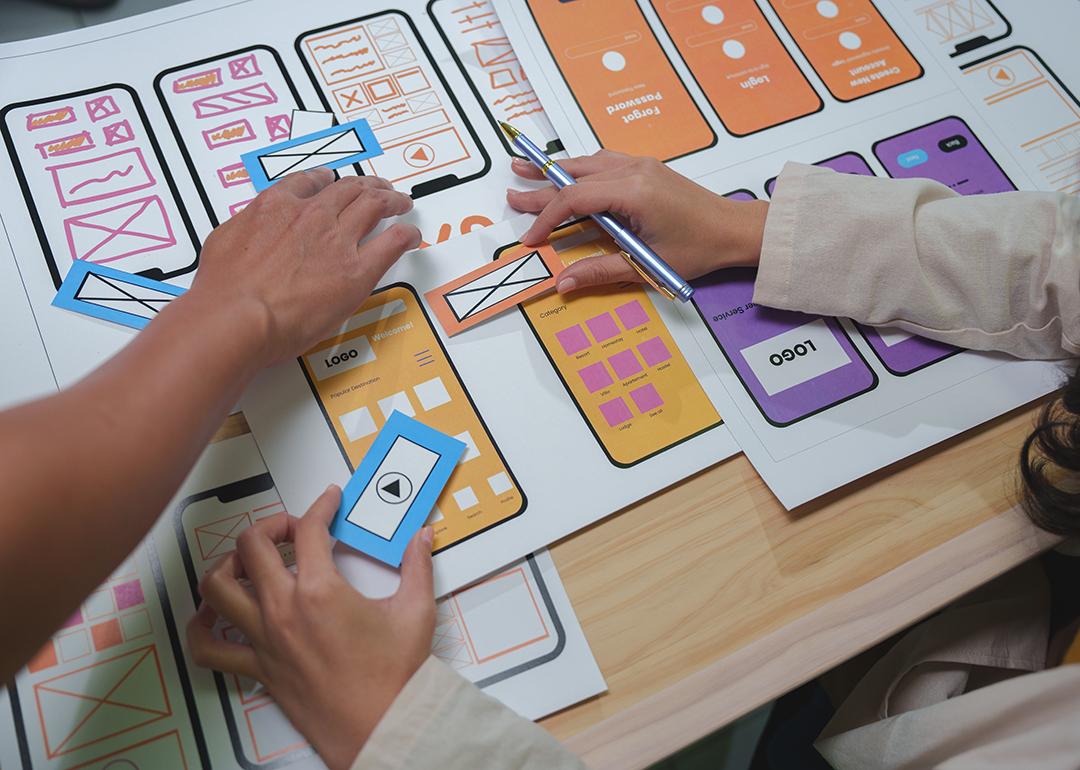 Web designers arranging cutouts to visualize a mobile app interface project.