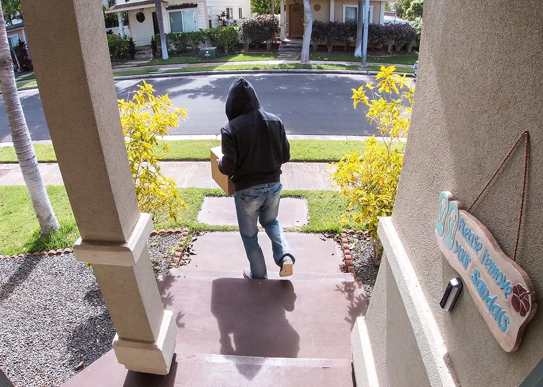 A surveillance camera-view of a package thief walking away from a porch after taking a package.
