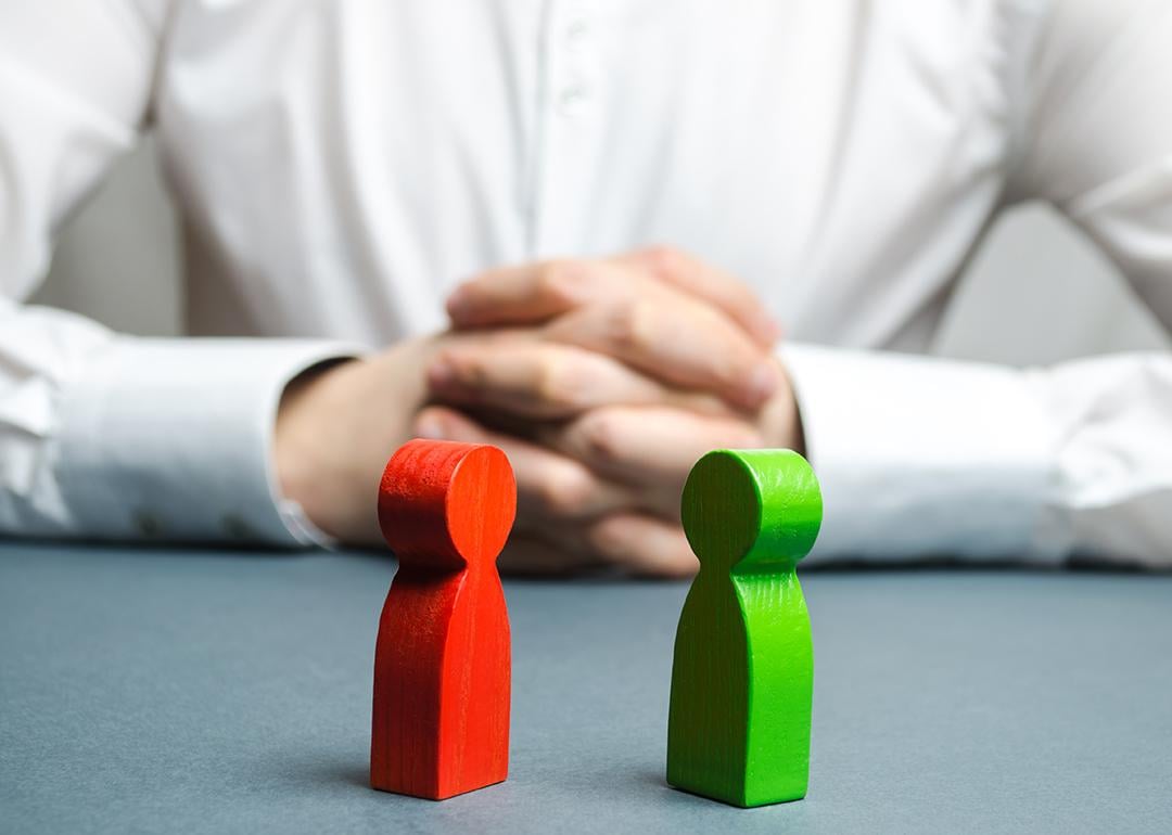 An arbitrator visualizing conflict situation between people depicted by two wooden figures.