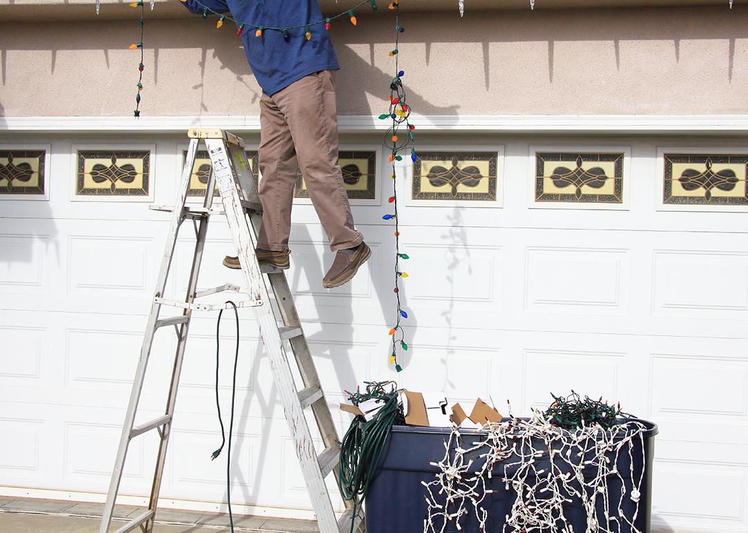 A man on a ladder carefully removes Christmas lights in their home.