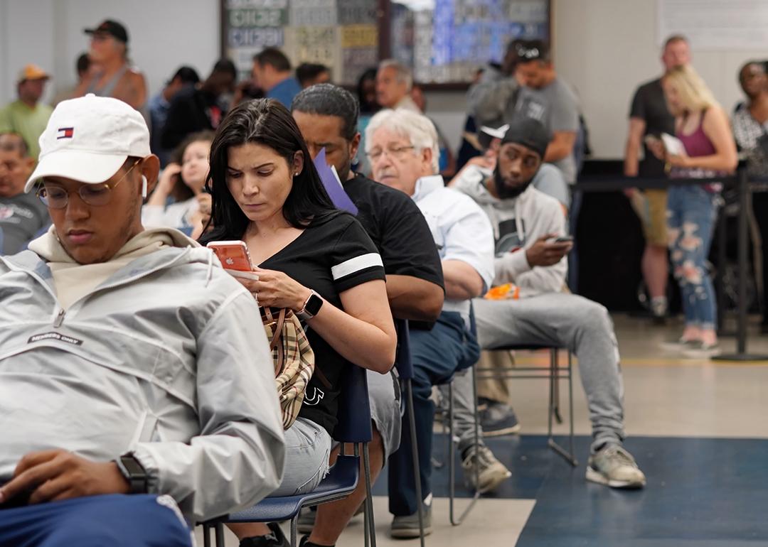 People seated for a queue where most are waiting by being on their phones.