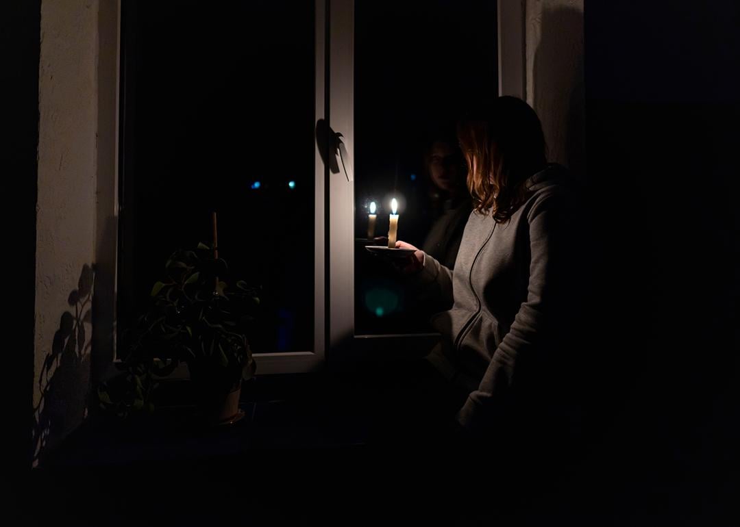 A woman standing by the window holding a candle during a power outage.