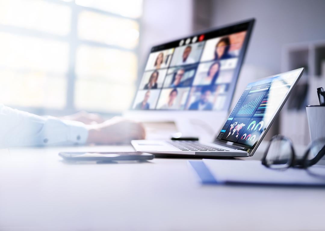 An employee's laptops at work displaying dashboards and a virtual video call.