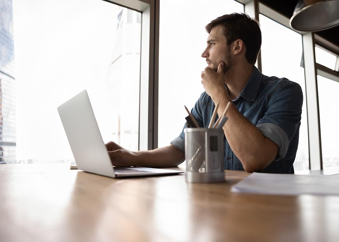 A male professional looking out the office window, pondering on work decisions.