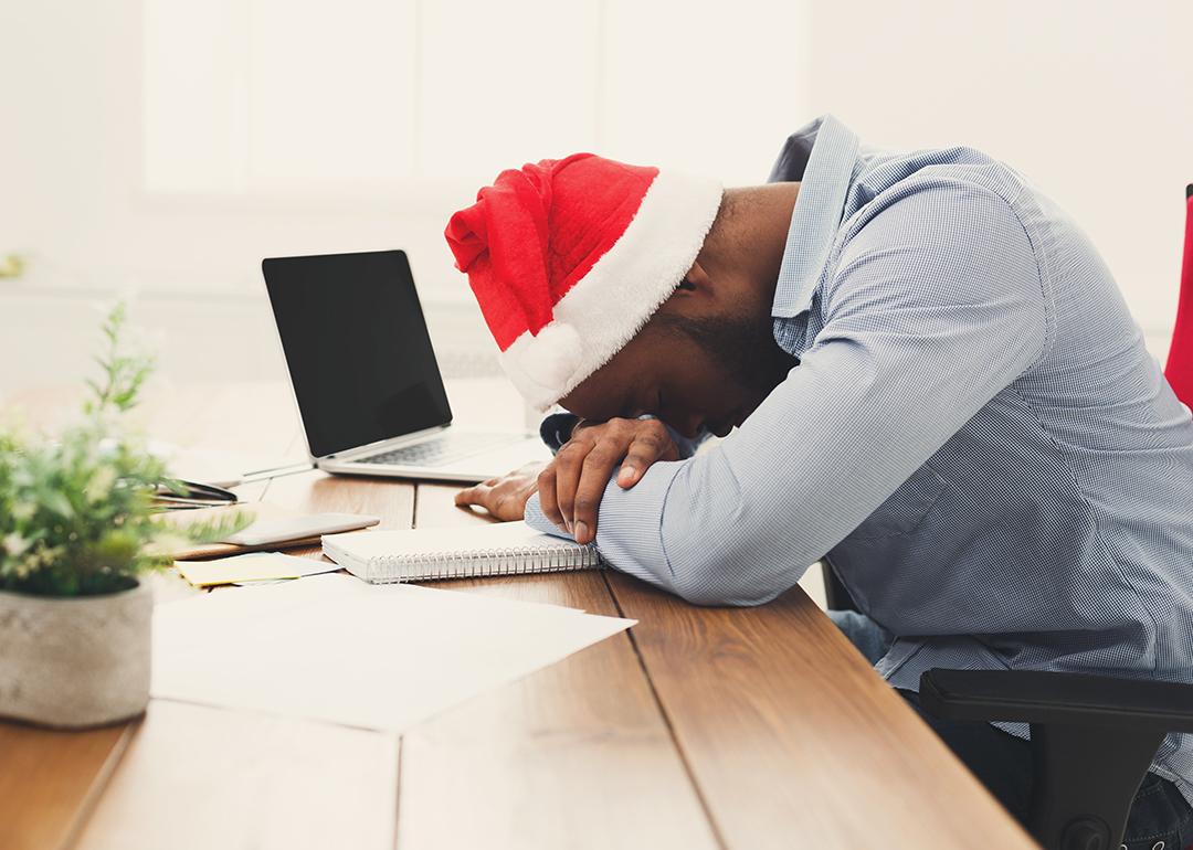 A tired businessman wearing a Christmas hat while asleep at work.