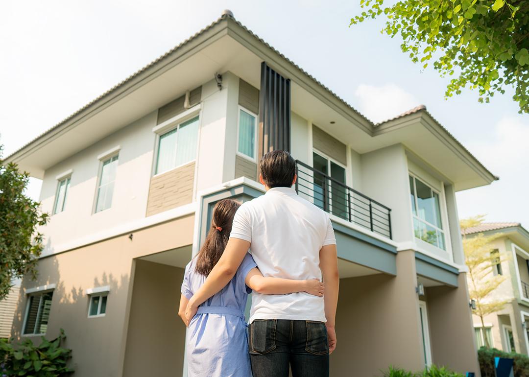 Back portrait of a young couple standing in front of their newly-bought home.
