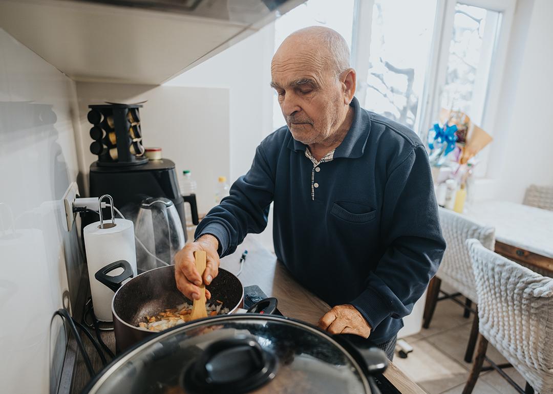 A senior man cooking a dish in his brightly-lit kitchen at home.