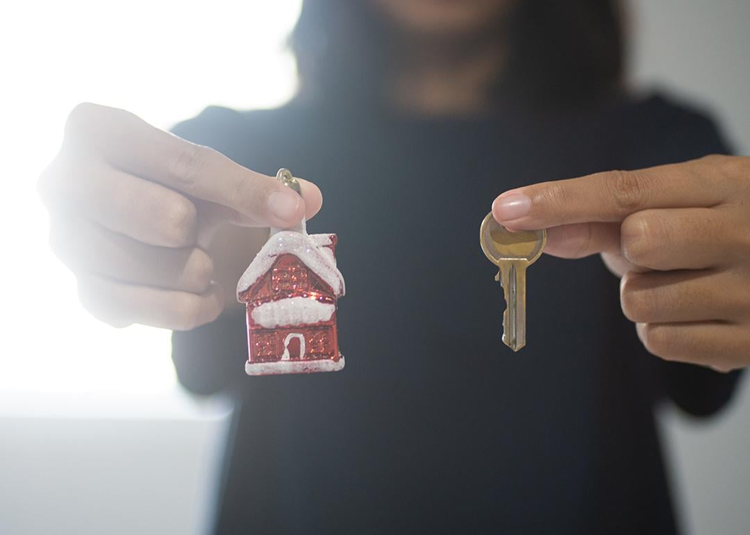 A woman holding a small figure of a Christmas home with her right hand and a house key with her left.