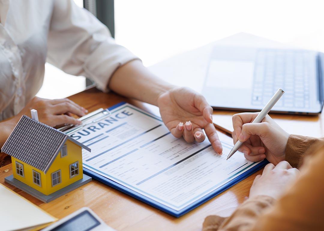 Two people whose faces are not visible review paperwork, representing a real estate broker agent presenting form customer to sign for insurance agreement.