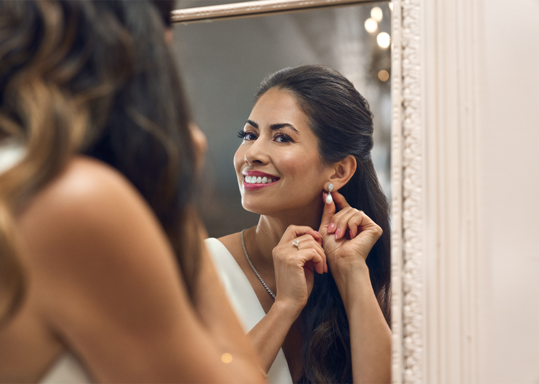 A woman looking at the mirror putting on her earrings.