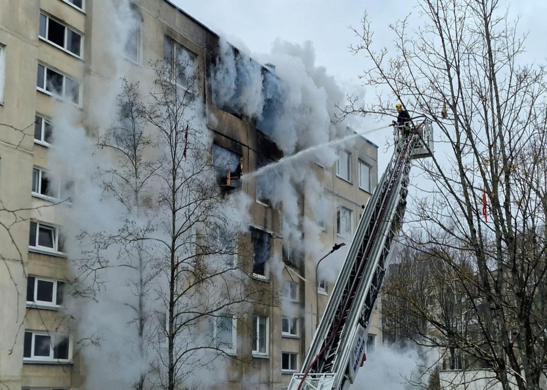 A firefighter on a lift sprays water from a hose into an apartment building as smoke pours out.. 