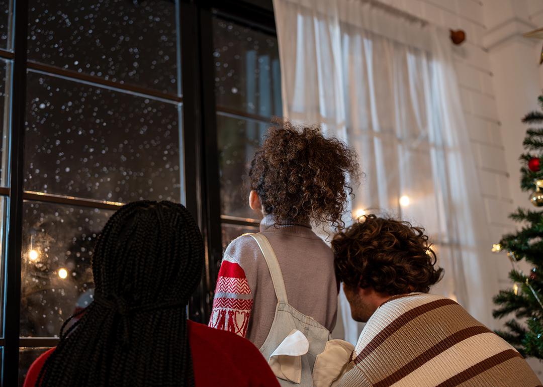 A family looking at the window to see snowfall at night.