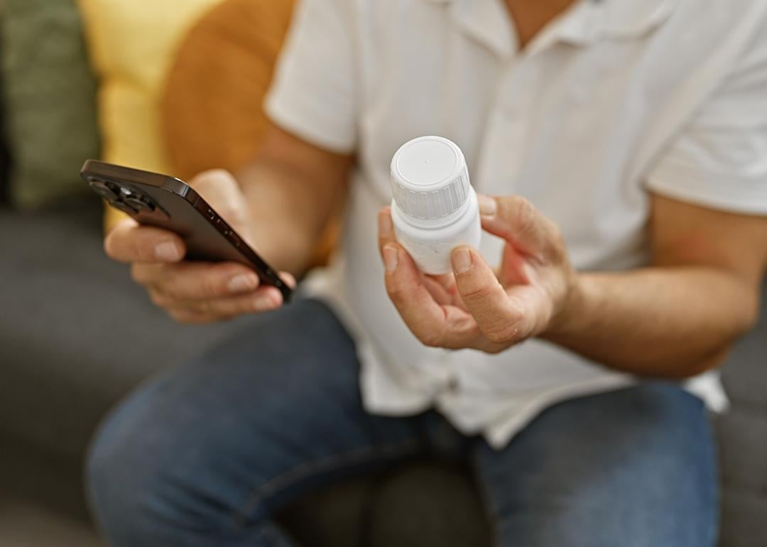 Person holding a prescription medicine bottle and checking info using smartphone.