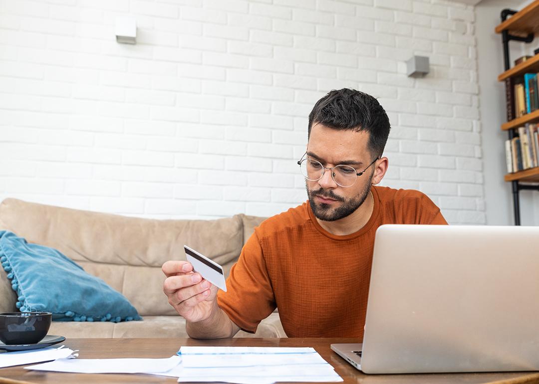 A stressed man reviewing credit card and utility expense documents at home.