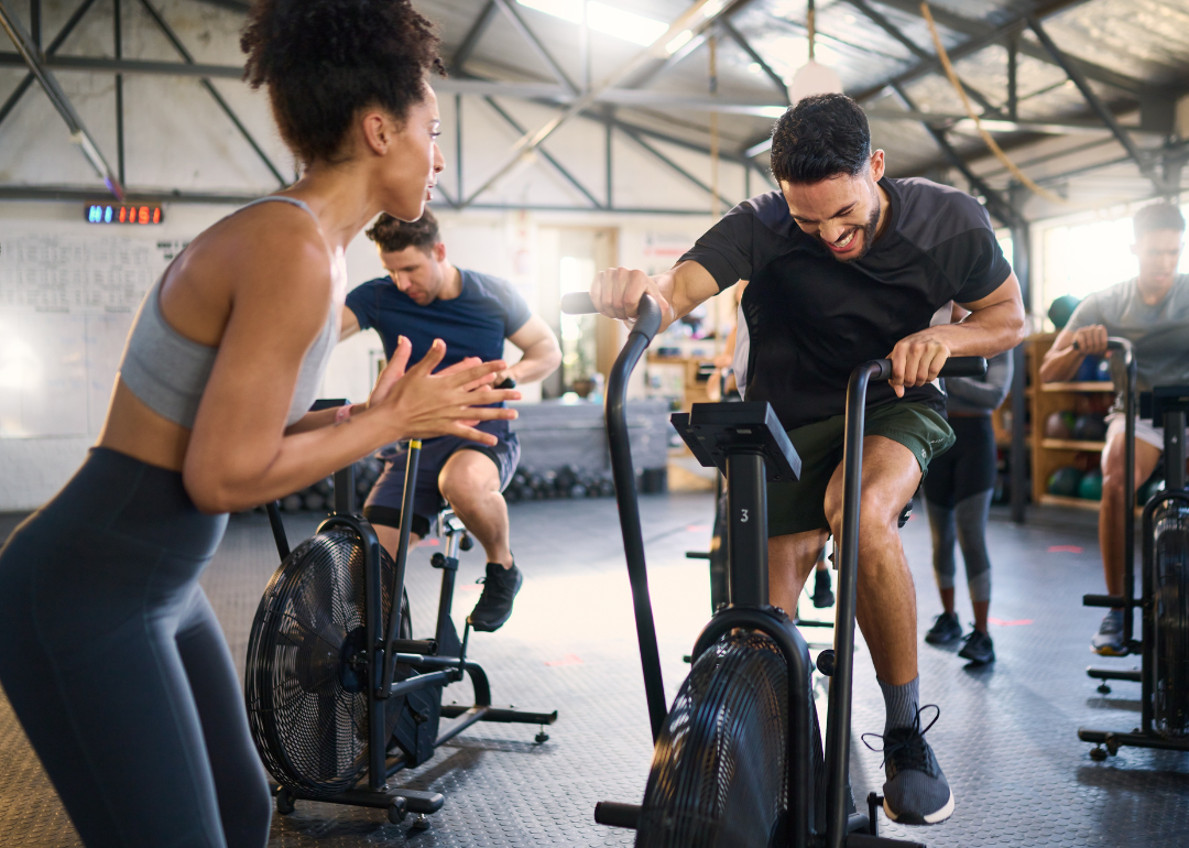 A trainer cheers on attendees of her spin class in a gym. 