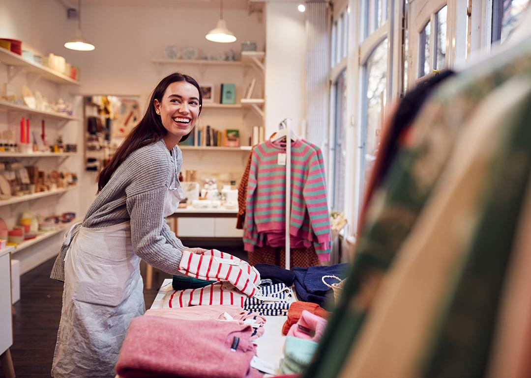 A female business owner arranging stock clothing for her store's window display.