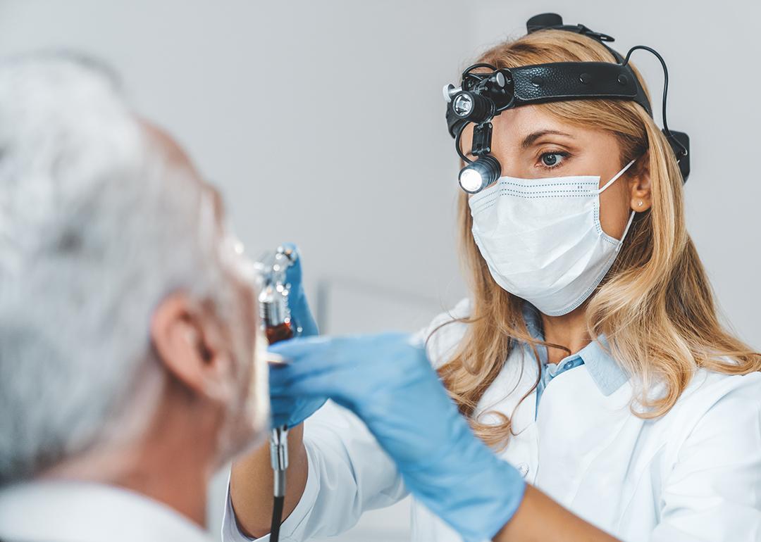 Close up of a female otolaryngologist making an examination of a senior patient's oral cavity.