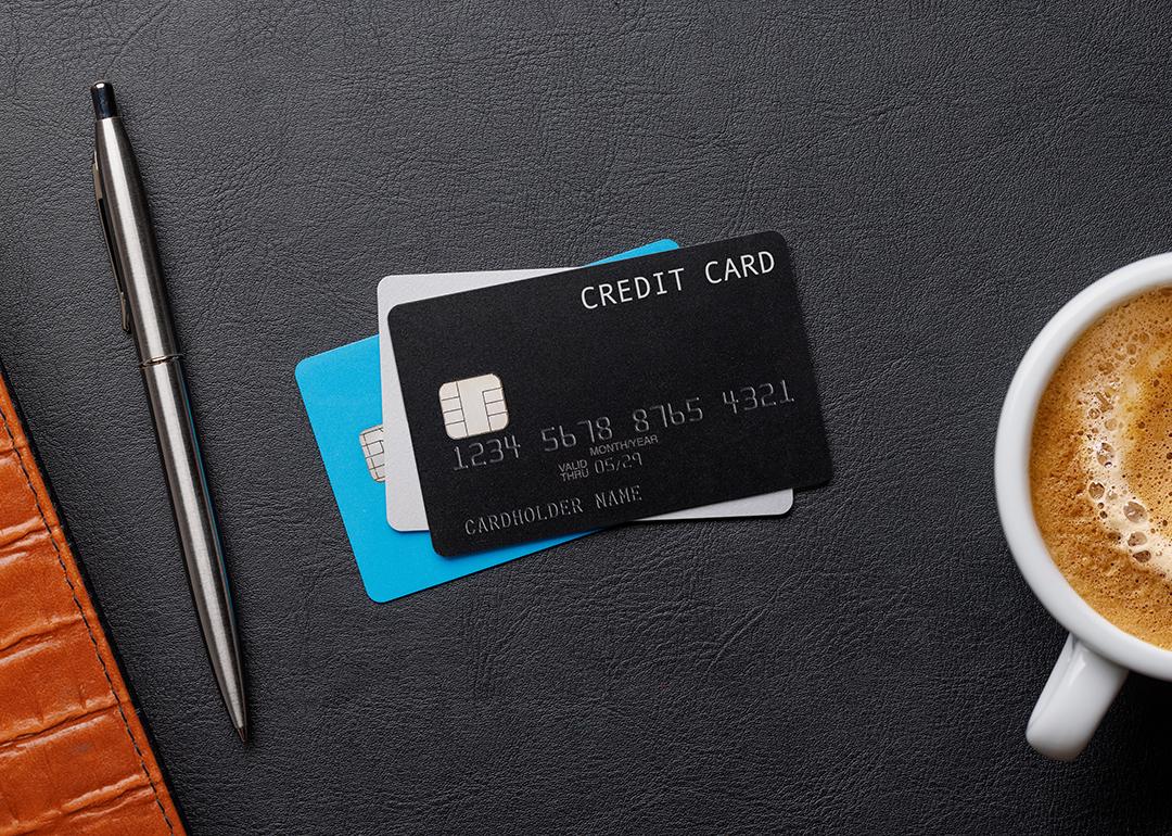 A flat lay of a stack of credit cards with a pen and cup of coffee on each side.