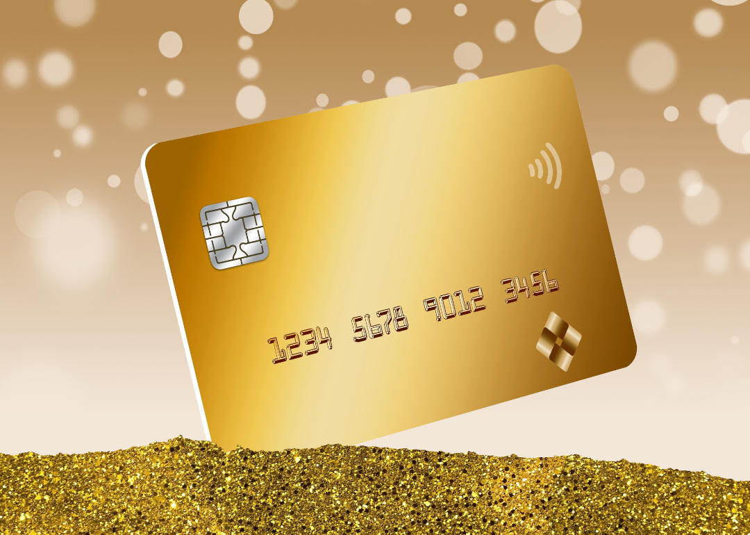 A gold credit card is seen in a pile of gold dust with bokeh circles in the background in a 3D illustration.