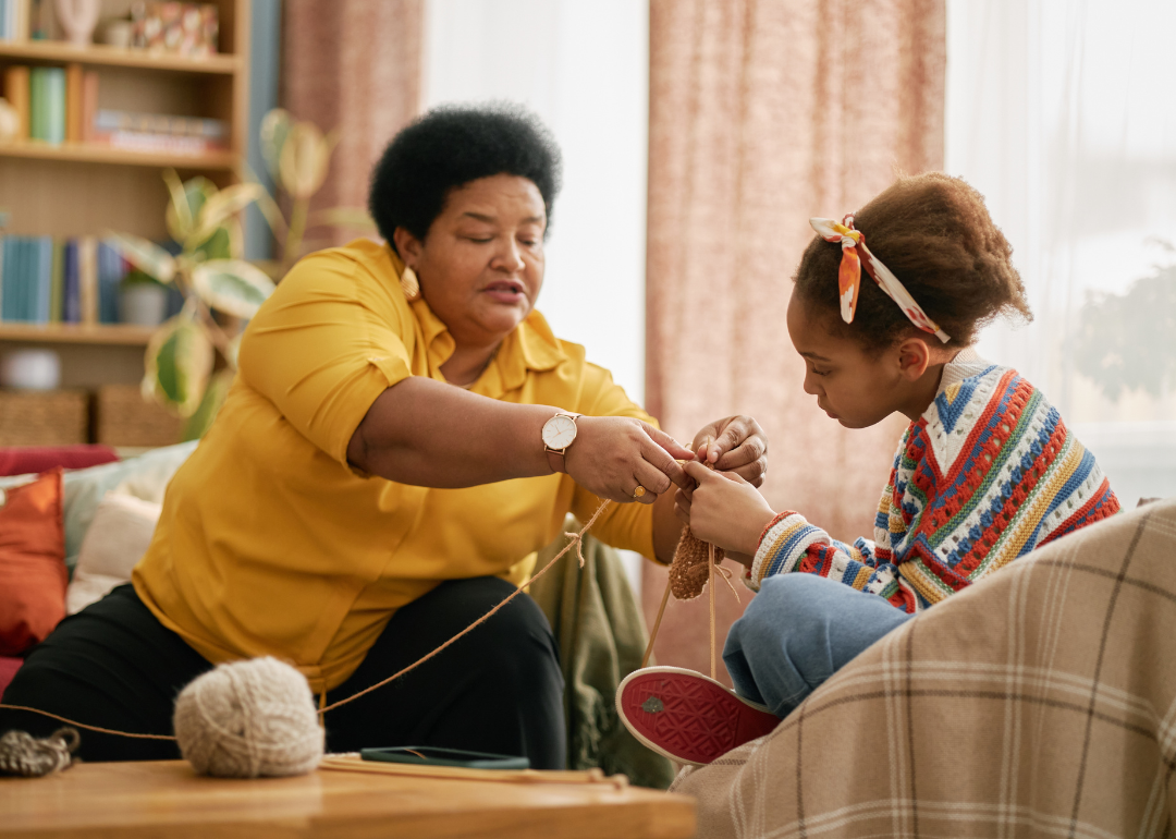 An older woman and a young girl sit in a living room as they wind yarn.