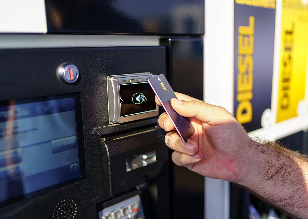 Hand of a person paying using card by the fuel pump at a gas station.