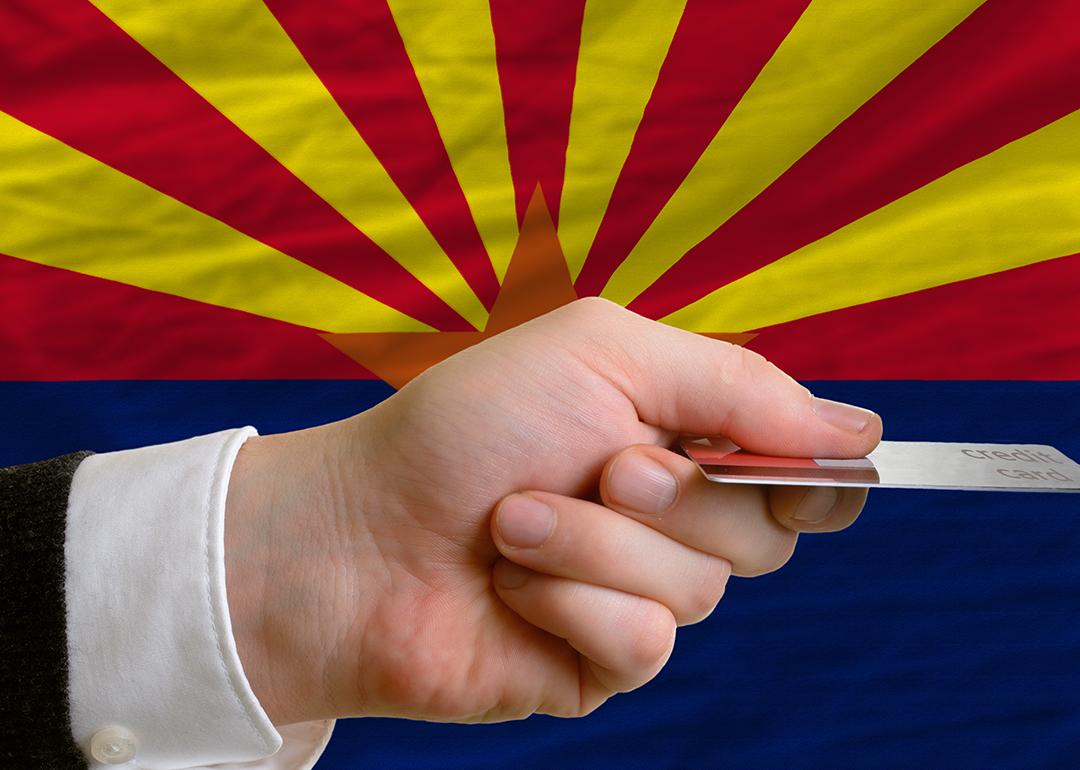 A person's hand holding a credit card with a background of Arizona's flag.