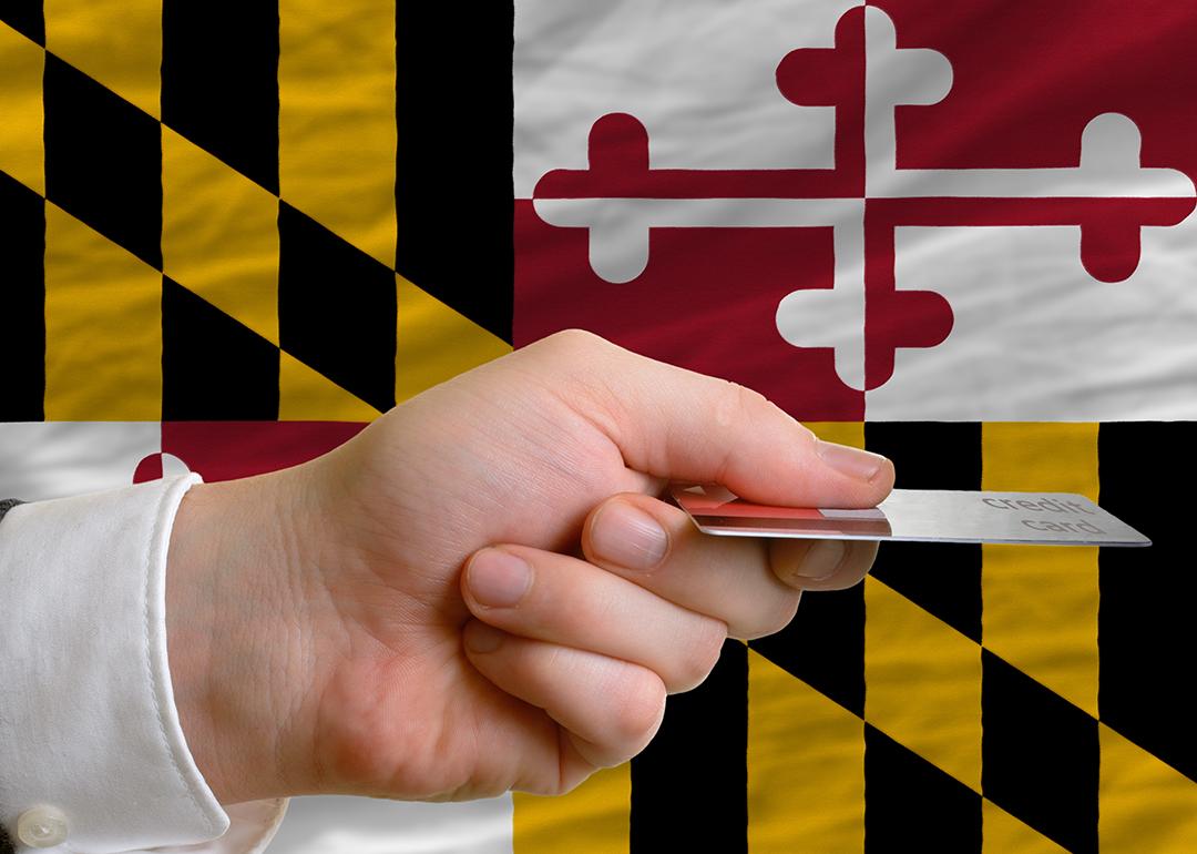 Person's hand holding a credit card with a background of Maryland's flag.