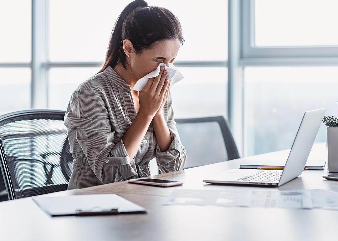 A sick businesswoman blowing her nose at work.