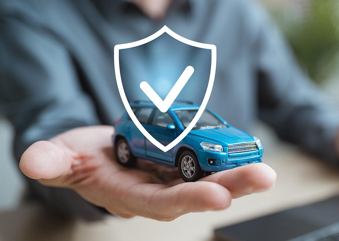 Person holding a small figure of a car illustrated with a shield as a concept of car insurance.