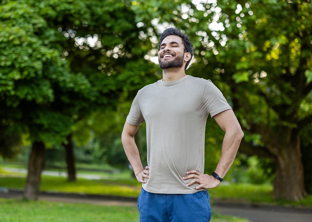 A sporty young man standing outdoors with hands on hips, smiling after an exercise.
