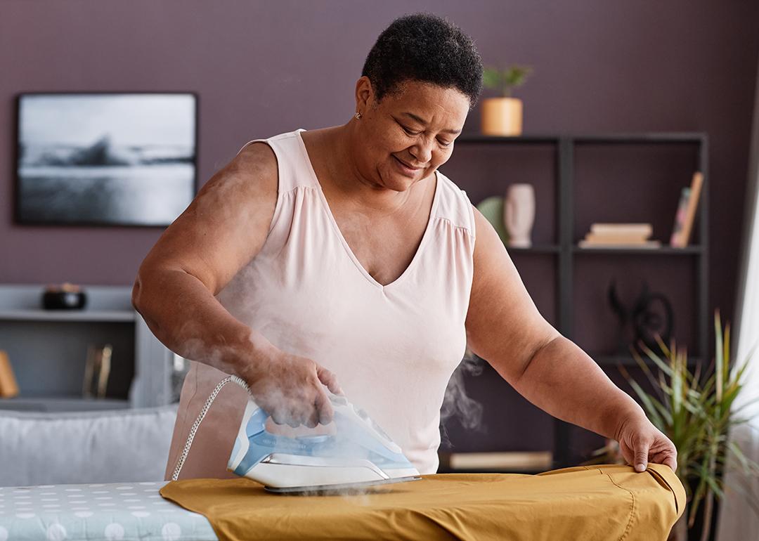 A senior woman happily ironing clothes at home.