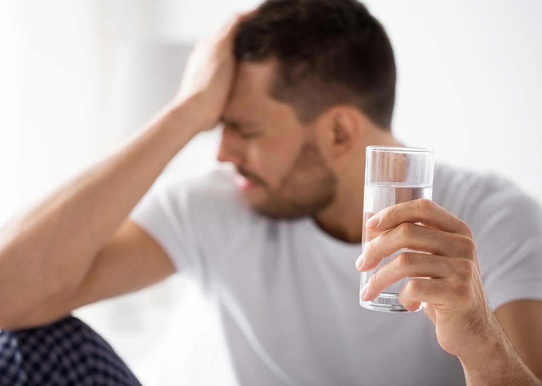 Man experiencing hangover holding a glass of water.