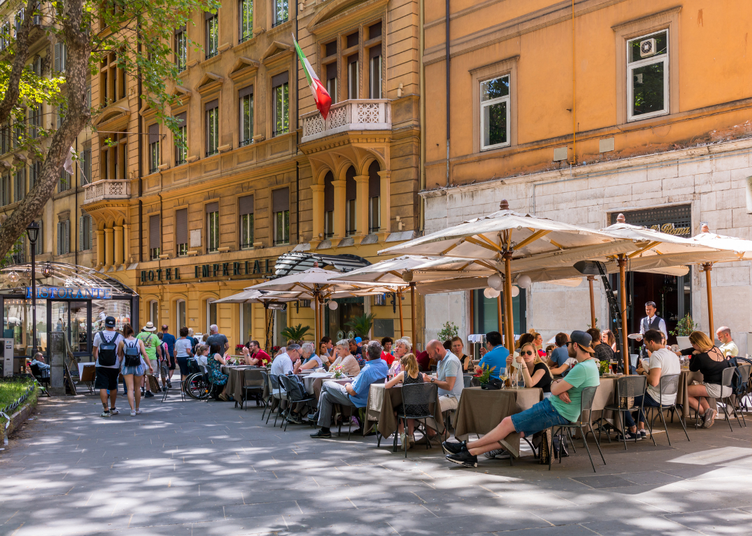 Tables under umbrellas filled with people outside of restaurants in Rome. 