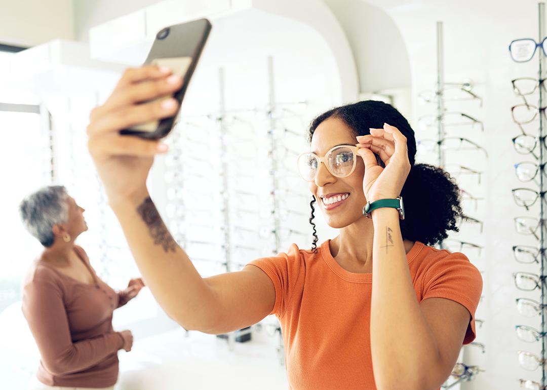 A young woman trying on eyeglasses in a shop and taking a selfie.