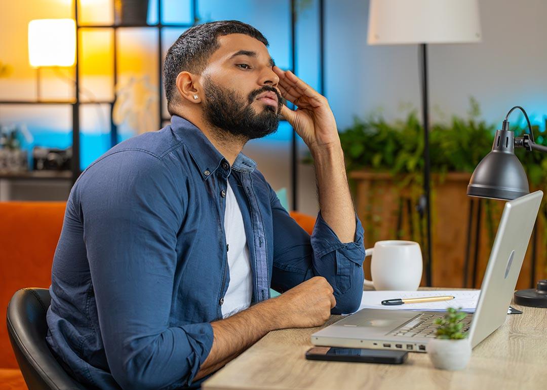 Man sitting at desk in modern colorful room looking at computer with an expression of distrust.