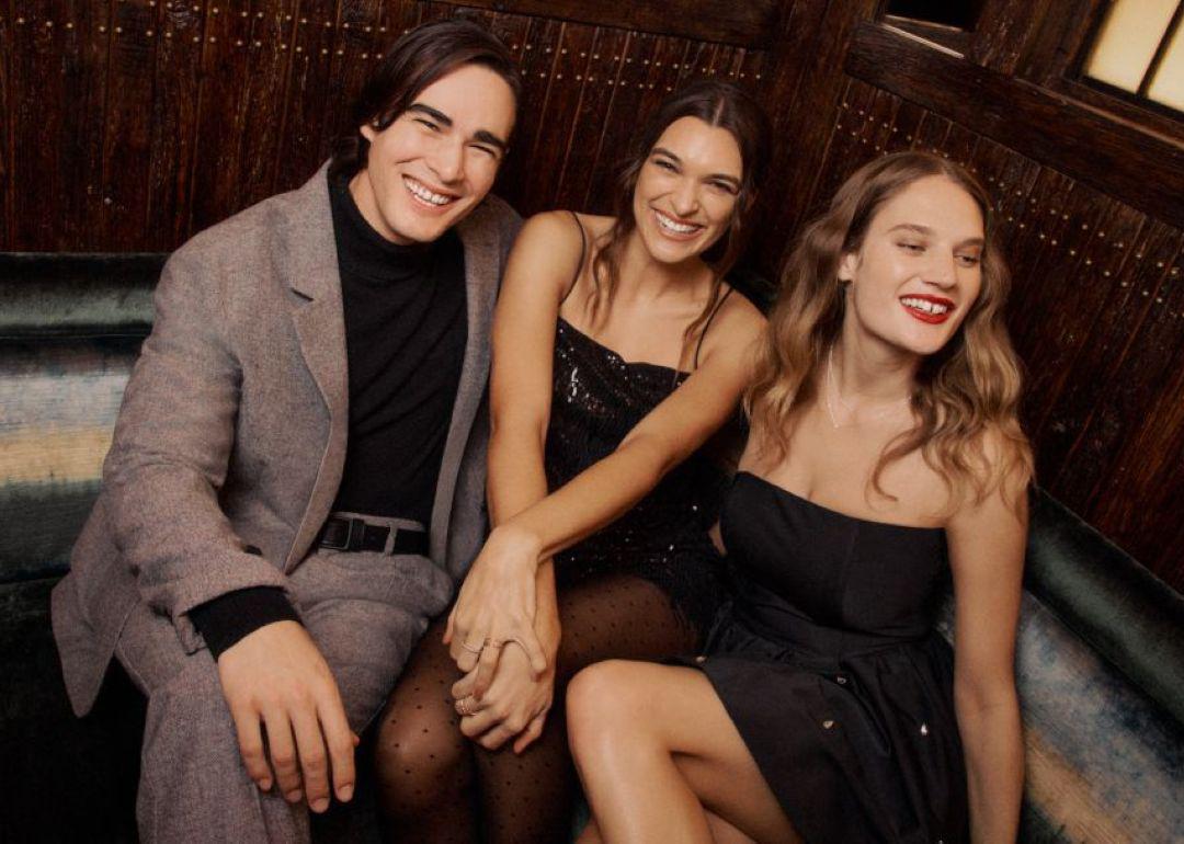 A group of three young personalities happily posing and sitting on an events sofa during a holiday celebration.