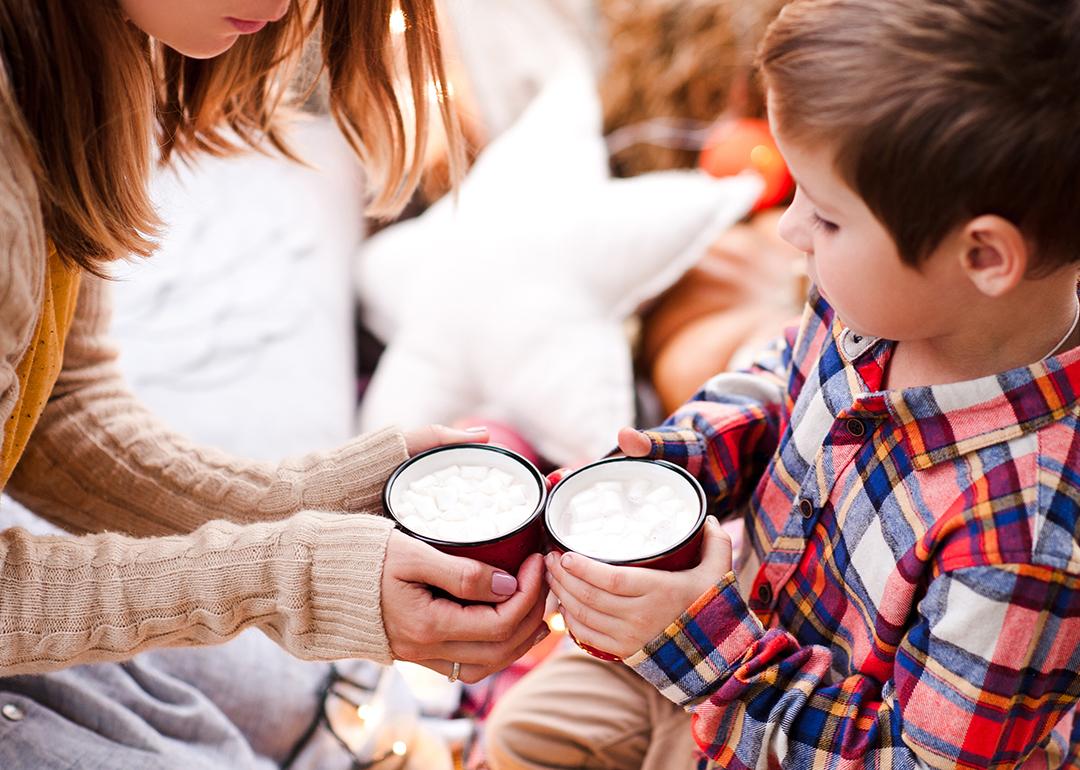 A young boy holding a cup of hot chocolate with his mother.