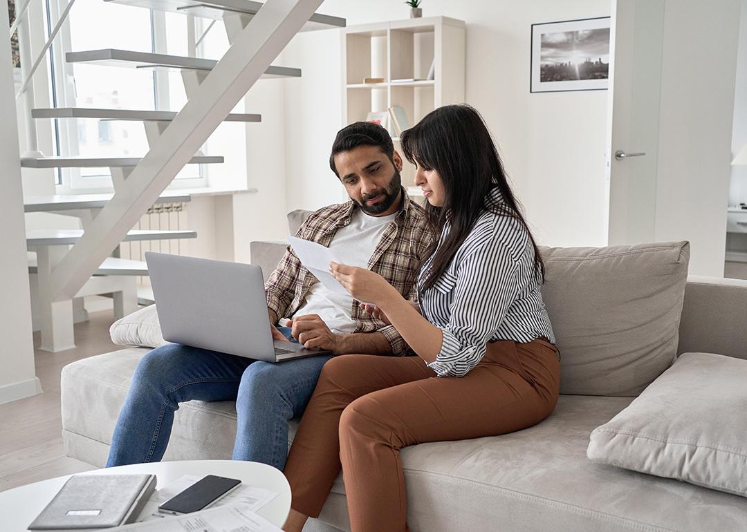 A couple sitting together on a sofa and reviewing bills.