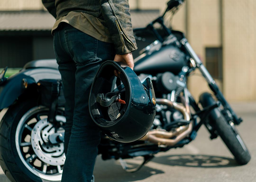 Close up of person holding motorcycle helmet with Harley type motorcycle in the background.