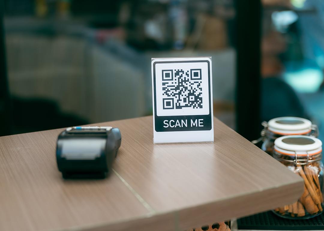 A 'scan me' QR code sign and payment terminal on a cafe reception table.