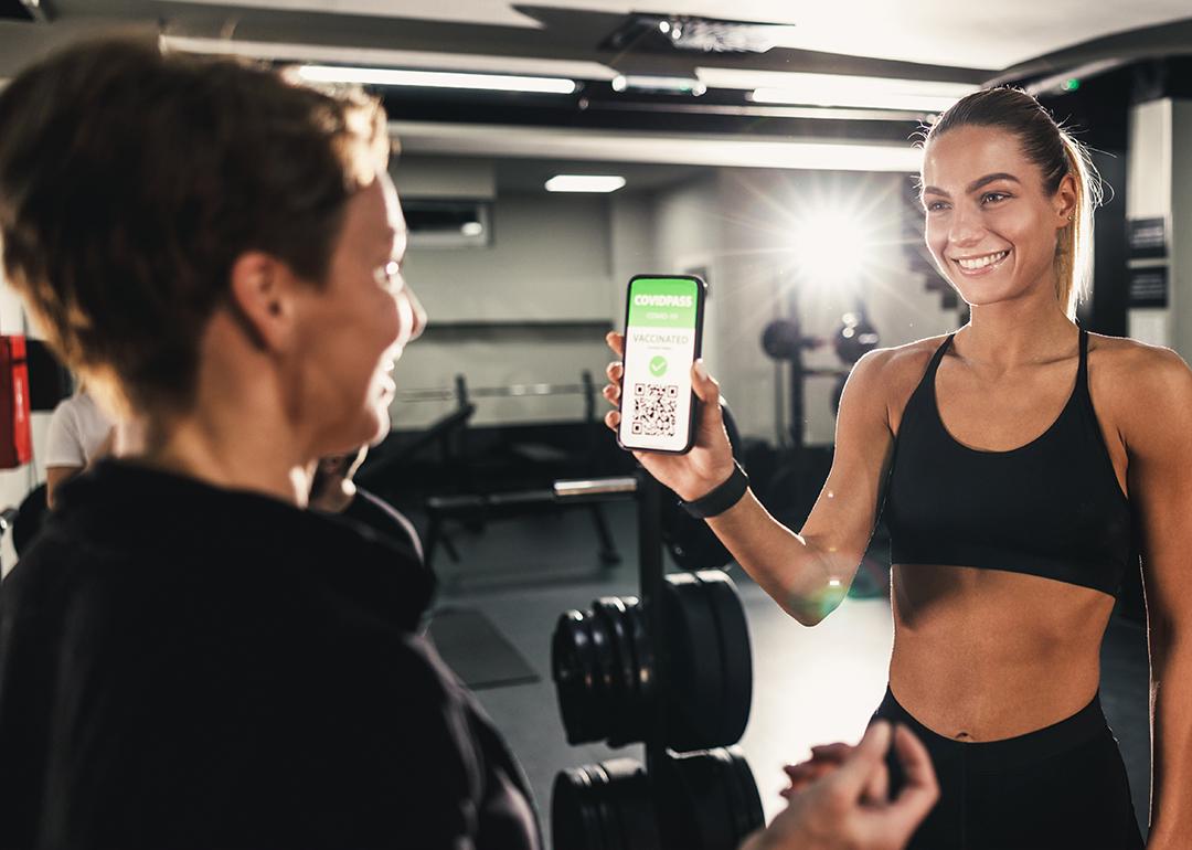 A female gym client showing a gym employee her QR code proof of COVID-19 vaccination.