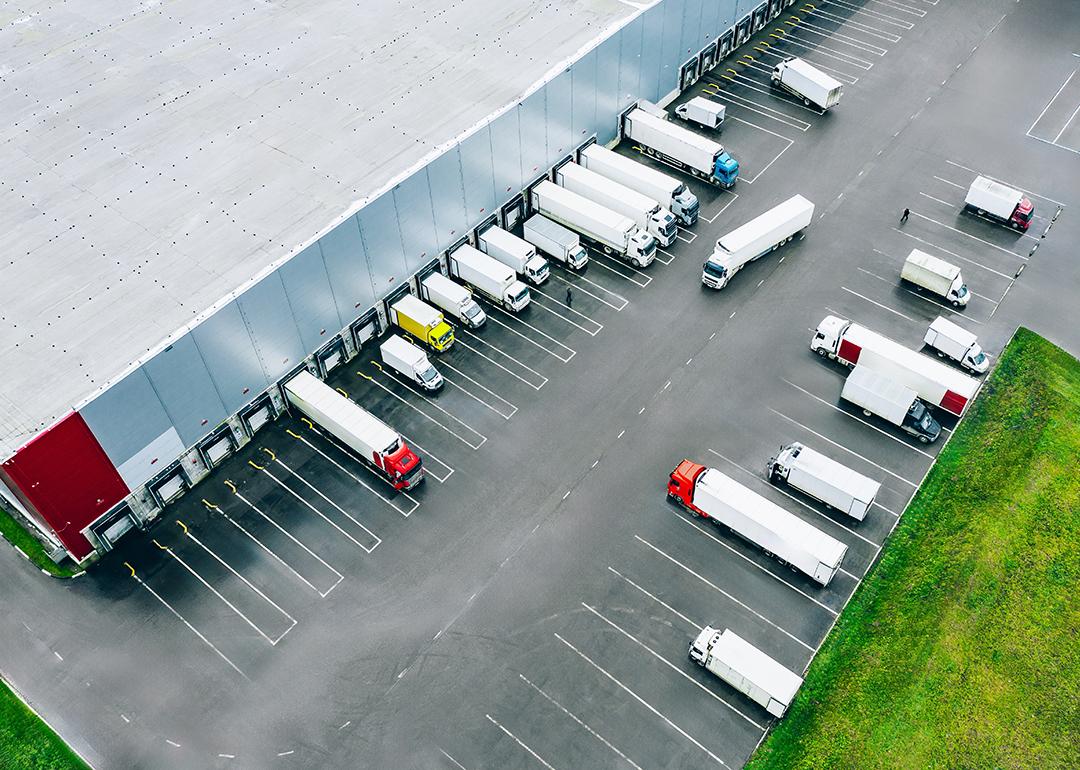 Aerial view of logistic trucks lined up at the loading docks of a large distribution warehouse.