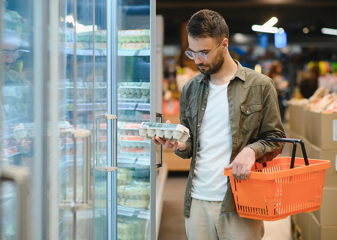 A young man checking eggs from a grocery store shelf.